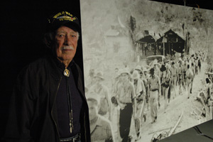 Pedro "Pete" Gonzalez by a picture of himself (in foreground, left, black pants) in Bataan death march