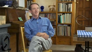 A man sitting on a chair in front of a bookcase.