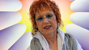 A woman with red hair in front of a colorful background.