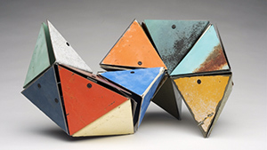 A group of colorful geometric sculptures on a gray background.