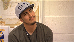 A man sitting in a classroom with a hat on.