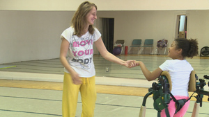 A woman shakes hands with a young girl in a dance studio.