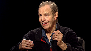 A man sitting in a chair with his hands in his pockets.