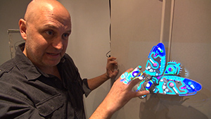 A bald man looking at a blue butterfly on a wall.