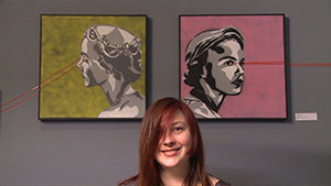 A woman smiling in front of two paintings.