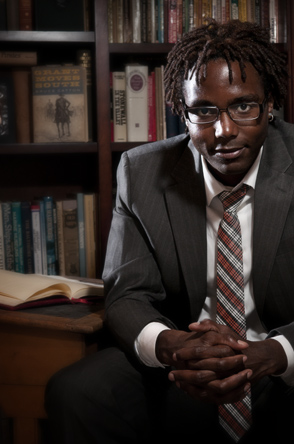 A man in a suit sitting in front of a bookcase.