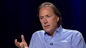 A man in a blue shirt is talking into a microphone.