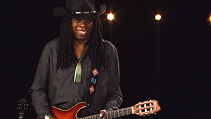 A man in a cowboy hat holding an orange guitar.