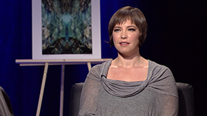 A woman sits in a chair and talks to a camera.