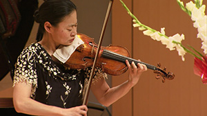 A woman playing a violin in front of flowers.