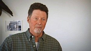 A man in a plaid shirt is standing in front of a wall.