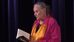 A woman reading a book in front of a curtain.