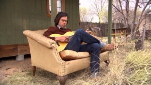 A man sitting in a chair playing an acoustic guitar.