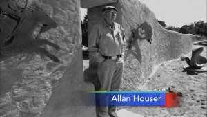 A black and white photo of a man standing in front of a sandstone wall.