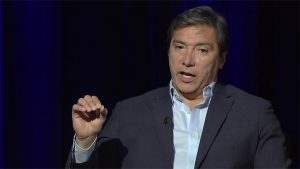 A man in a suit speaking into a microphone.
