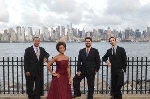 Four people standing in front of a fence with a city skyline in the background.