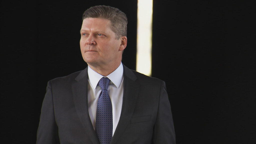 Robert K. Meya wearing a suit and standing against a black background