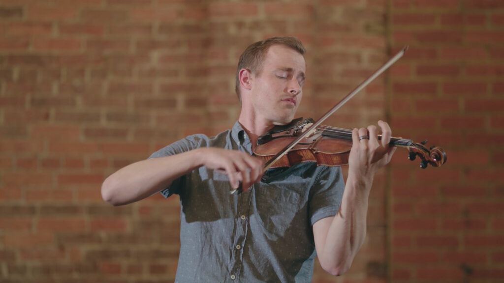 a man plays the violin in front of a brick background