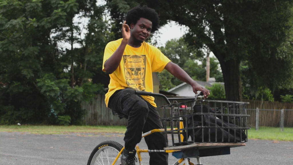 A person rides a bike waving at the camera