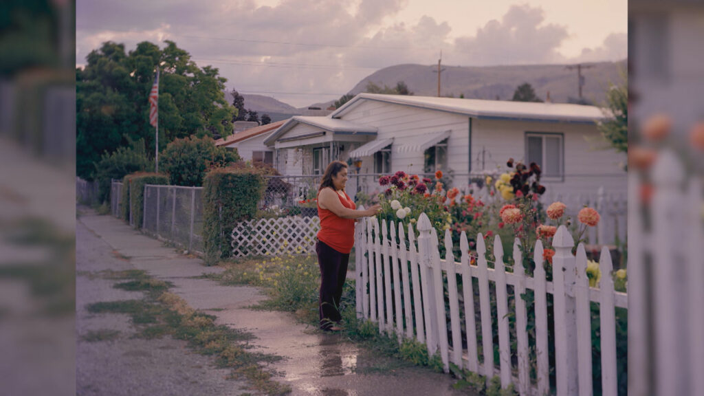 A person outside looking at flowers behind a white fence