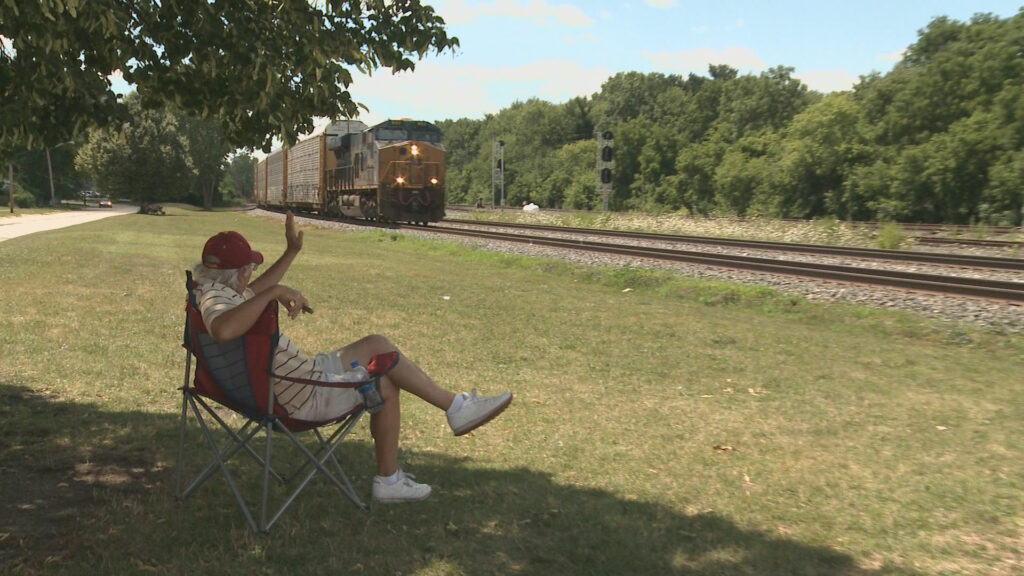 A person sitting in a chair waves at a passing by train