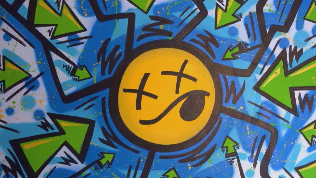 A spray painted smiley face with "x" eyes and green arrows pointing at it