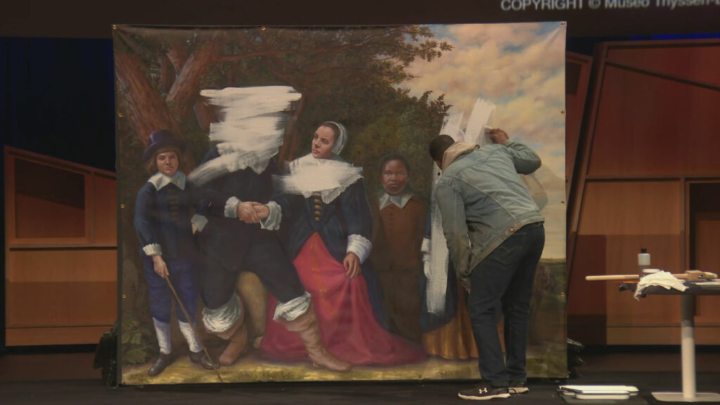 A person painting white over another painting of a group of people