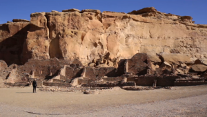 A man standing in front of a cliff with ruins in the background.