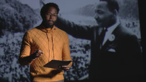Hakim Bellamy standing and giving a speech in front of Martin Luther King Jr.