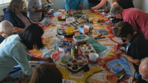 People crowding around a table working on a mosaic.