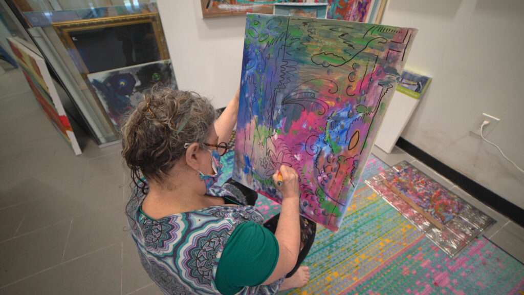 A woman sitting and holding a painting in her lap to paint on details.