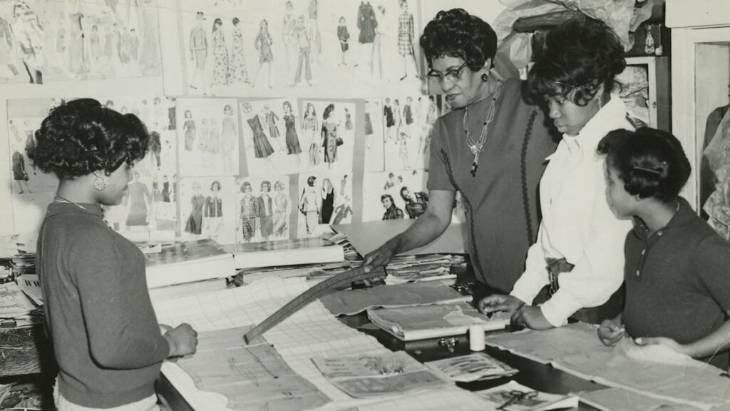 A black and white photo of a group of women looking at fashion designs.