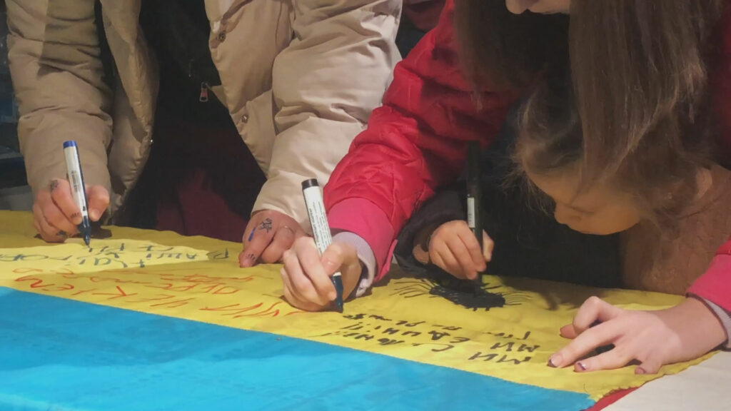 People with markers writing on the Ukrainian Flag.