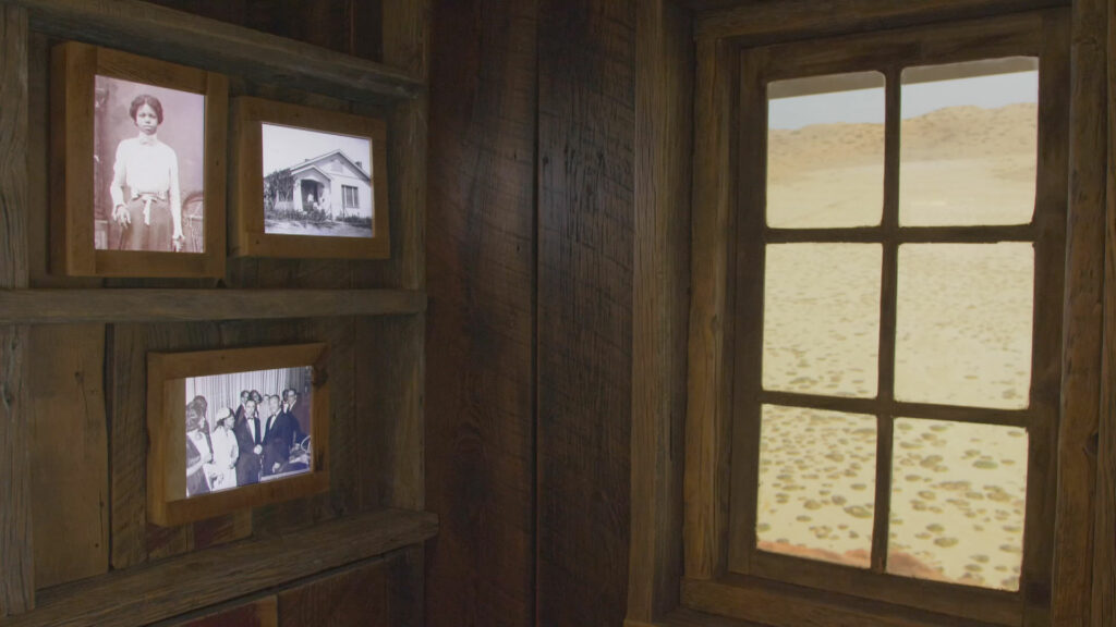 An exhibit featuring a window looking out at the desert and screens that appear to be changing photographs on the wall.