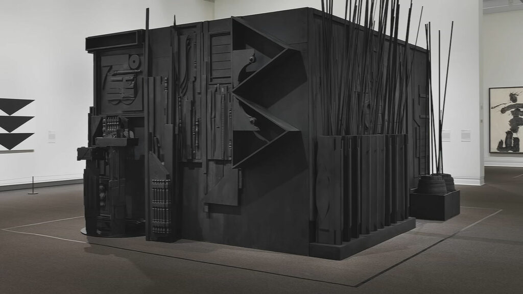 An art piece that looks like a charcoal black building made out of various objects. 