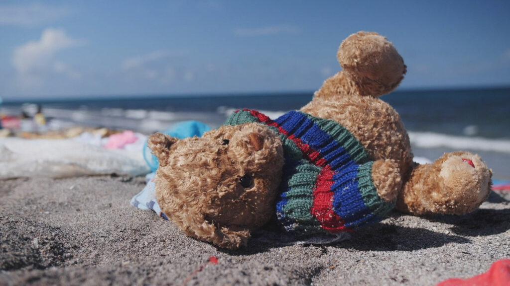 A lone teddy bear washed up on a beach.