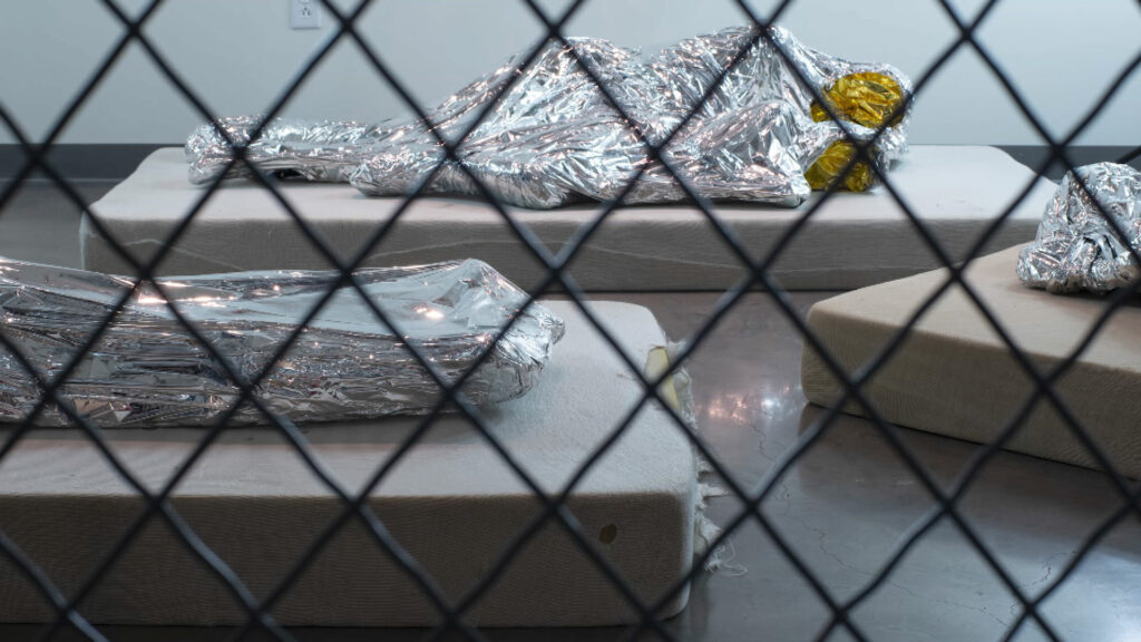 Delilah Montoya's work depicting people huddled together under tin foil blankets on mattresses behind a fence.
