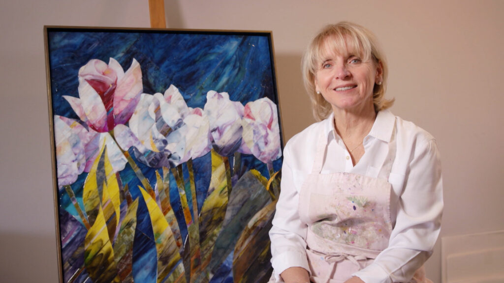 Terri Albanese sitting next to her mosaic of flowers made from glass.