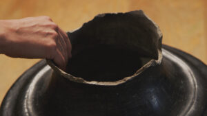 A persons hand grabbing the opening of a clay vase.