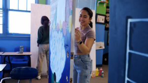 A woman is painting a door in a classroom.