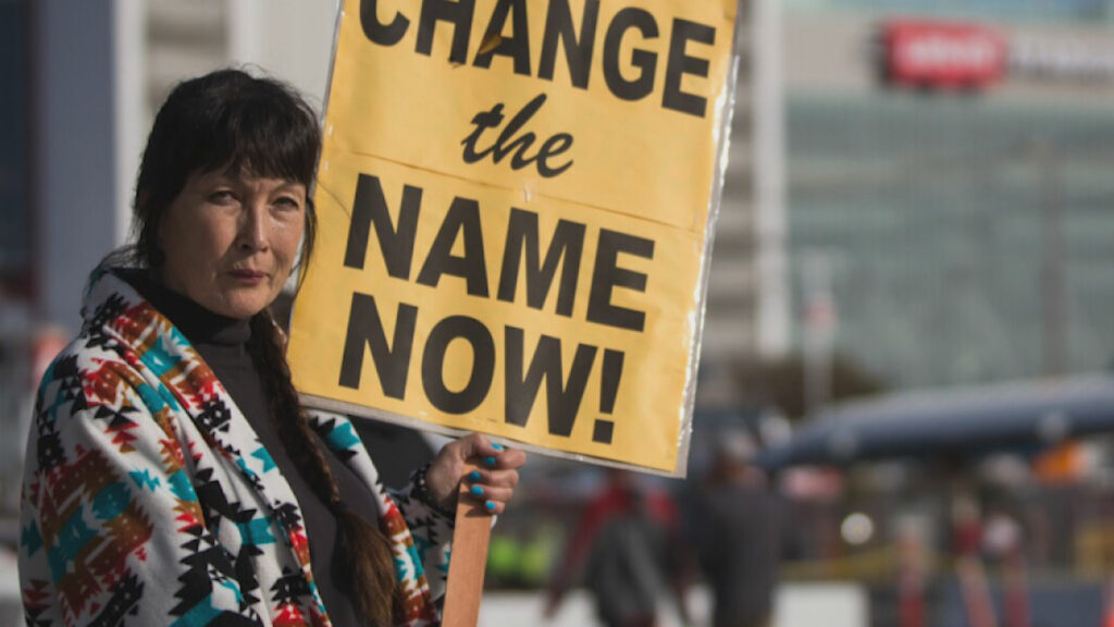 A woman holding a sign that says change the name now.