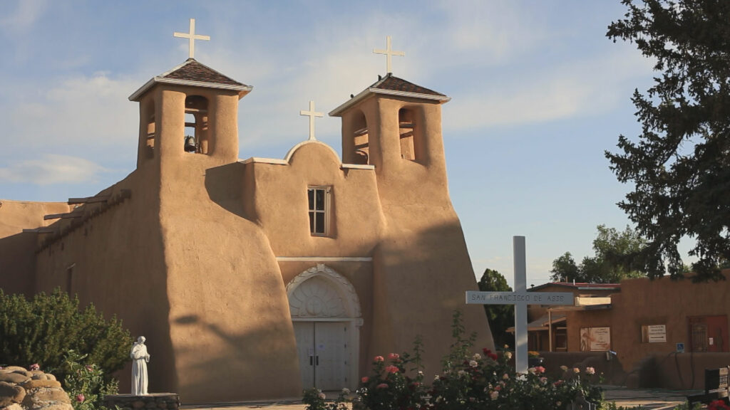 An adobe church with a cross in front of it.