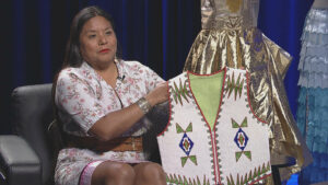 A woman sits in front of a mannequin wearing a vest.