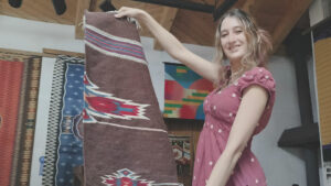 A woman is holding up a rug in a room.