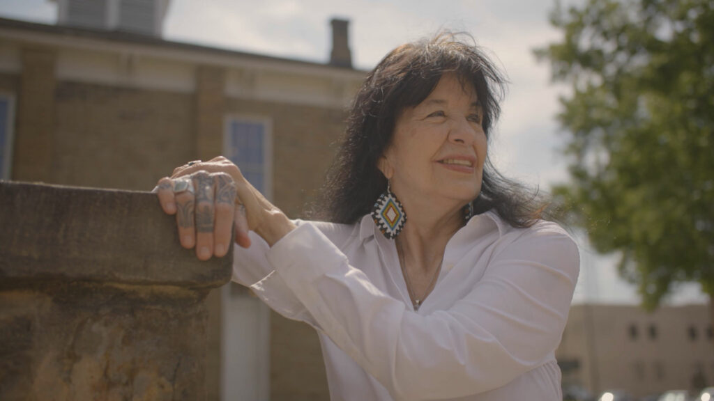 A woman wearing a white shirt leaning against a wall.