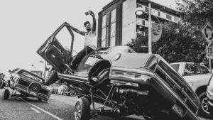 A black and white photo of a man on top of a car.