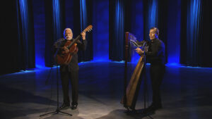 Two men playing guitar and harp in a stage.