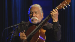 A man playing an acoustic guitar in front of a microphone.