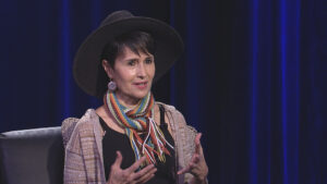 A woman wearing a hat and scarf is sitting in a chair.