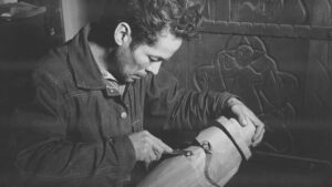 A black and white photo of a man carving a piece of wood.